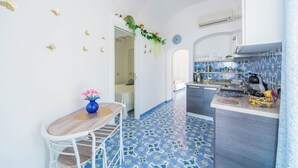 A kitchen with a blue tiled floor, white walls, and a wooden dining table with a vase of flowers. - YourHome - Lorena Maria House Positano (Positano)