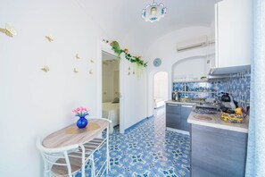 A kitchen with a blue tiled floor, white walls, and a wooden dining table with a vase of flowers. - YourHome - Lorena Maria House Positano (Positano)