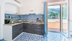 A kitchen with blue patterned tiles, a sink, and a view of a mountainous landscape through a sliding glass door. - YourHome - Lorena Maria House Positano (Positano)
