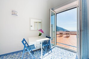 A room with a white desk, blue chairs, a potted plant, and a view of a terrace with chairs. - YourHome - Lorena Maria House Positano (Positano)