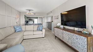 Ein modernes Wohnzimmer mit einer Couch, einem Fernseher, einem Schrank und einer Küche im Hintergrund.