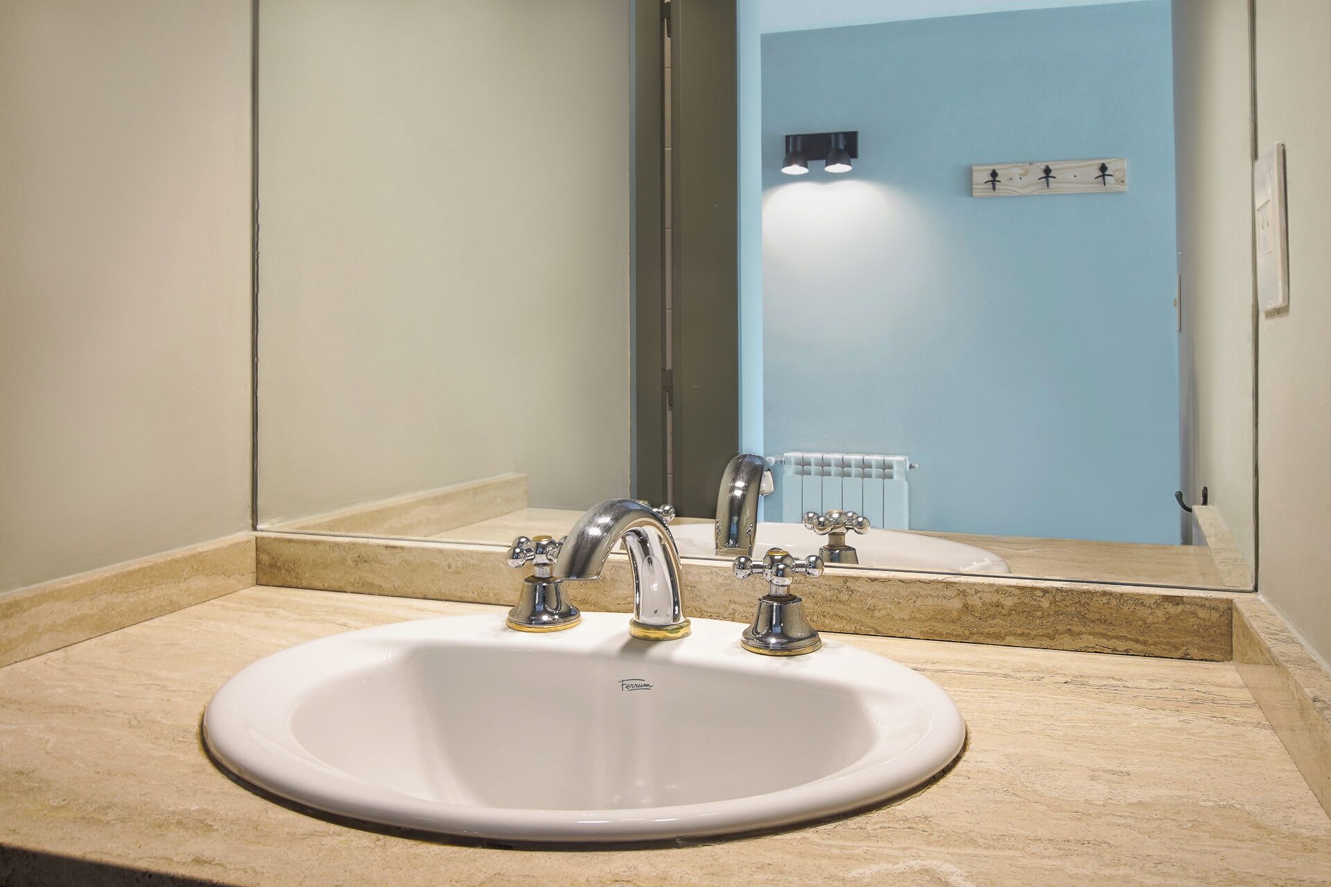 Ein Badezimmer mit einem weißen Waschbecken, zwei Wasserhähnen, einem Spiegel und einer blauen Wand.