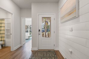 Un pasillo con una puerta blanca, piso de madera y vista a una piscina exterior.