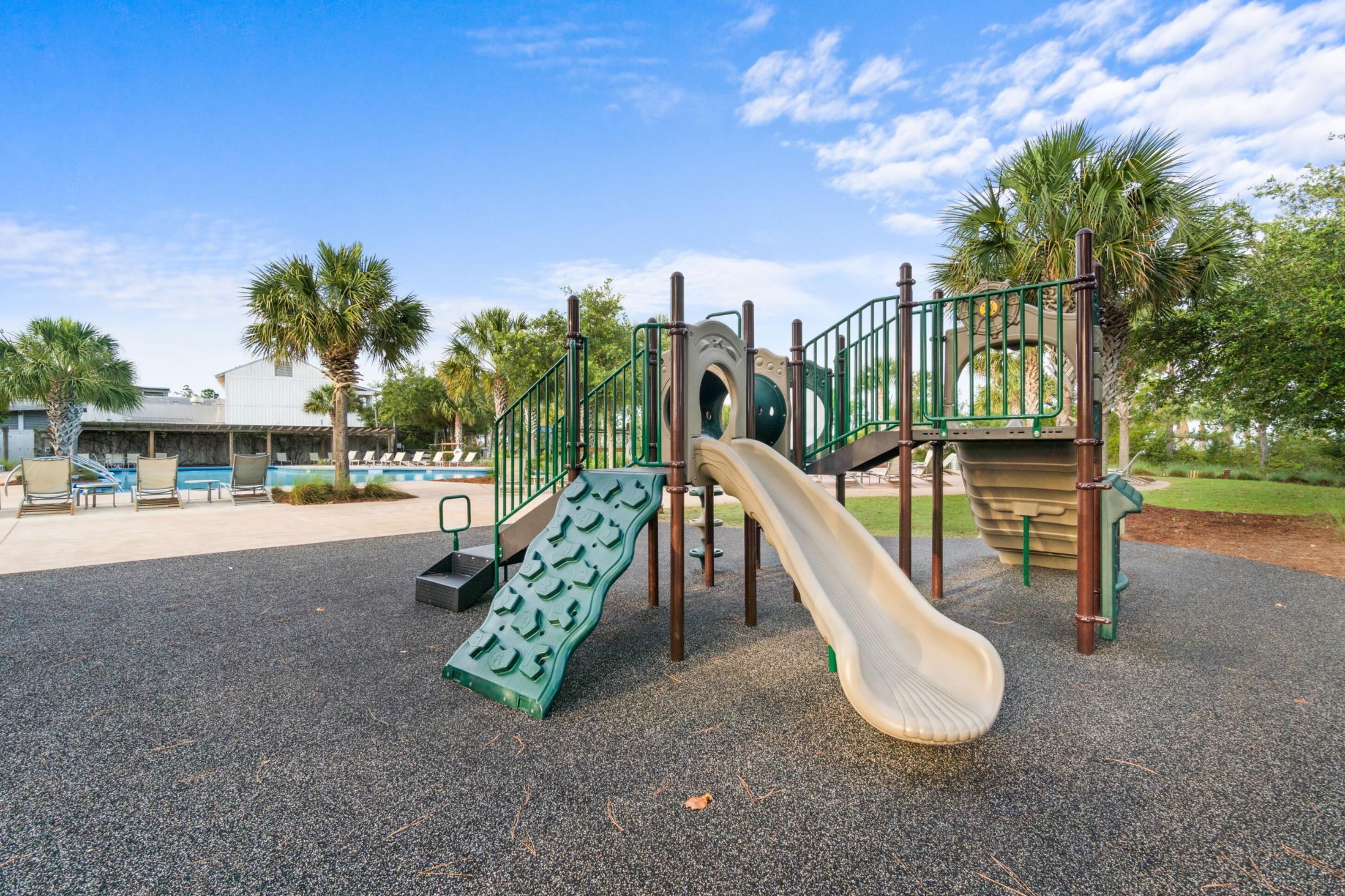 Un parque infantil con tobogán, estructuras para escalar y una zona de piscina con sillas de descanso.