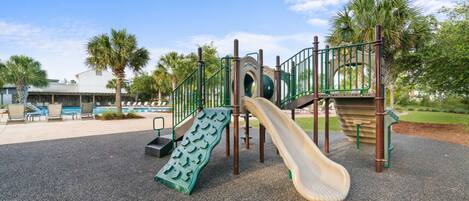 Un parque infantil con tobogán, estructuras para escalar y una zona de piscina con sillas de descanso.