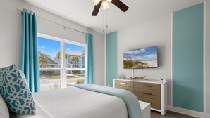 Un dormitorio con cama, escritorio, televisor y ventana con cortinas.