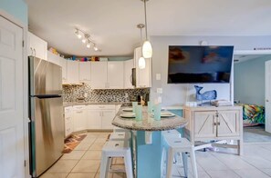 A modern kitchen with white cabinets, a stainless steel refrigerator, a granite island, and a flat-screen TV mounted above it. - Walk to Beach, Indoor/Outdoor Pools, Steps to Grocery (Ocean City)