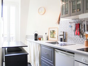 A kitchen with a sink, cabinets, a clock, and a framed picture on the wall. - Bright 35m² apartment with sunny balcony in Paris (Paris)
