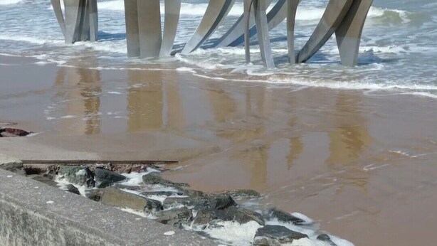 Une plage avec une barrière en béton et des sculptures métalliques abstraites.