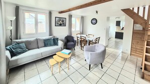 Un salon comprenant un canapé, des fauteuils, une petite table, une table à manger avec des chaises, une horloge et un escalier.