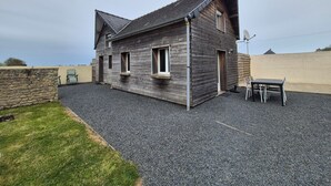 Une maison à deux étages avec un toit en pente, une allée gravillonnée et un petit patio comprenant une table et des chaises.