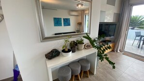 A modern living room with a large mirror, a white console table with potted plants, grey ottomans, and a TV.