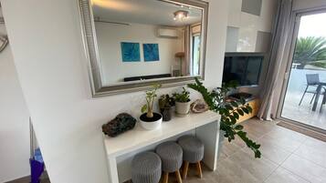 A modern living room with a large mirror, a white console table with potted plants, grey ottomans, and a TV.