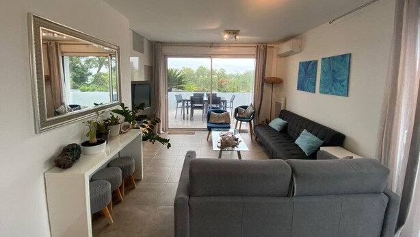A modern living room with a grey sofa, a coffee table, and a dining area with a table and chairs.
