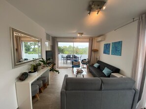 Un salon moderne avec un canapé gris, une table basse et un coin repas comprenant une table et des chaises.