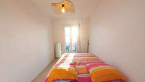 Ein schmales Zimmer mit einem Bett, einer Hängelampe und einem Fenster.