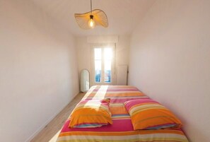 A narrow room with a bed, a hanging light fixture, and a window. - Sunny Flat with Sea-View Balcony (Les Sables-d'Olonne)