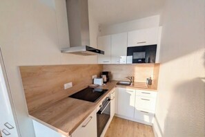A compact kitchen with a wood countertop, built-in oven, white cabinetry, and a microwave. - Sunny Flat with Sea-View Balcony (Les Sables-d'Olonne)