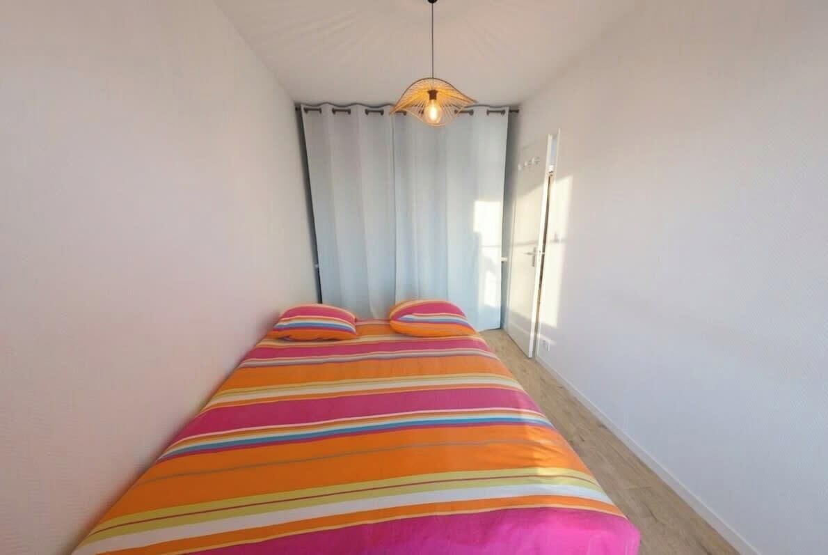 Una stanza piccola e stretta con un letto, una lampada a sospensione e una finestra con tende.