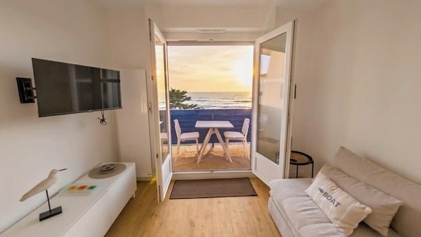 Ein Zimmer mit Fernseher, einer Couch, einem Esstisch mit Stühlen und Meerblick.