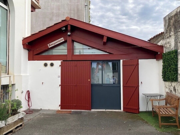 A building with a red roof, a dark blue door, and a small table and bench outside.