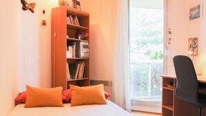Ein Schlafzimmer mit Bett, Bücherregal, Schreibtisch und Fenster.