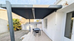 Ein überdachter Patio-Bereich mit Tisch und Stühlen, einem Betonboden und einer weißen Wand.