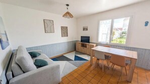 Ein Wohnzimmer mit einer Couch, einem Fernseher, einem Esstisch und einem Fenster.