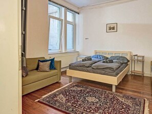 Ein Schlafzimmer mit Bett, Sofa, Fenster und Heizkörper.