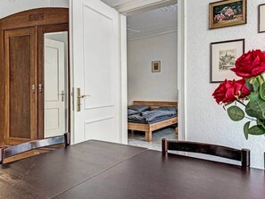 Ein Zimmer mit Holztür, einem Bett mit Holzgestell, einer weißen Wand mit gerahmten Bildern und einem Tisch mit Stühlen.