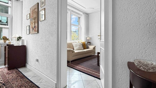 A hallway with a patterned rug, a sofa, and a window with a view.