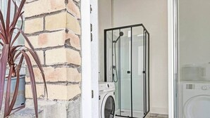 A laundry area with a washing machine and a glass-enclosed shower.