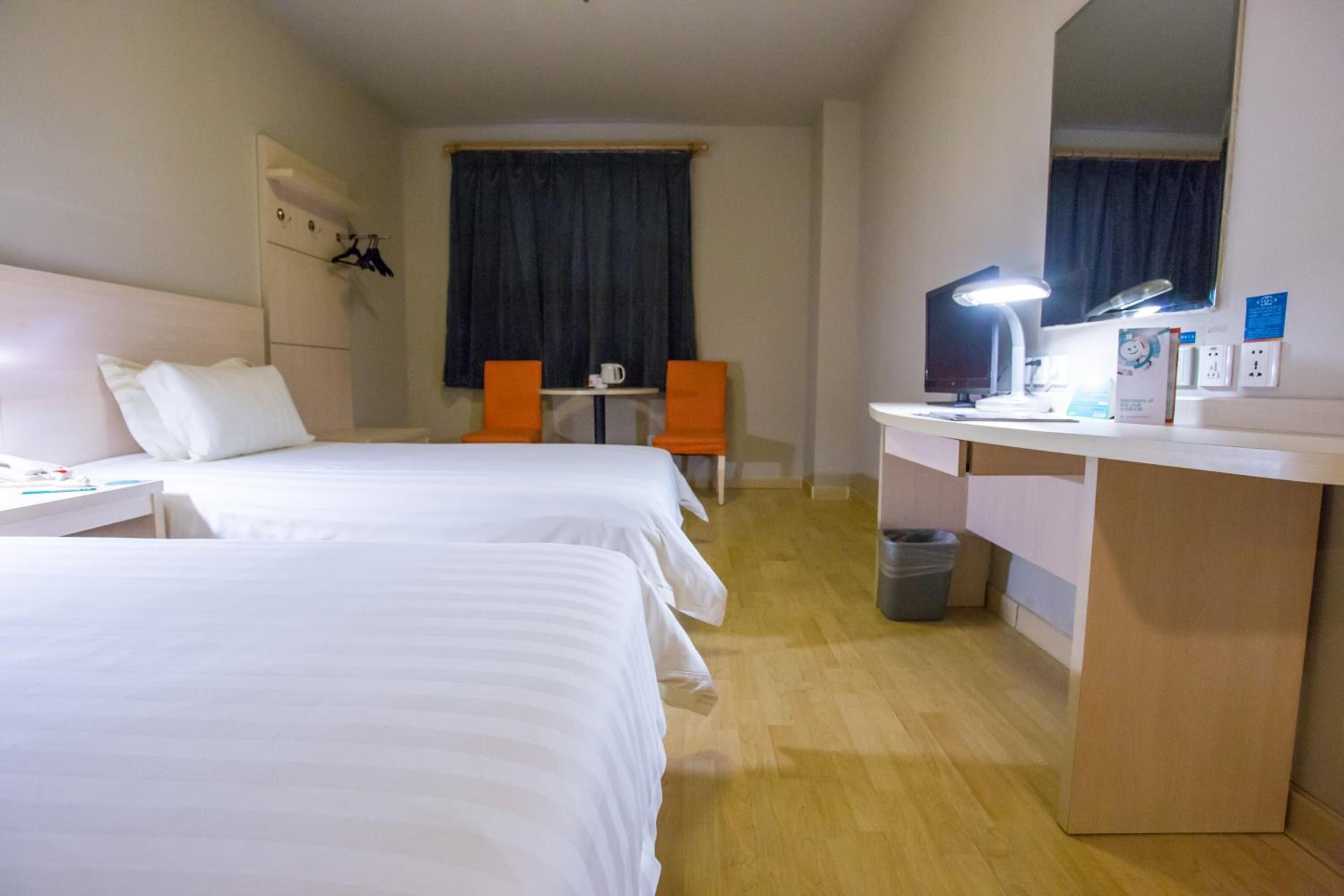 Habitación de hotel con dos camas, un escritorio, una silla, un espejo y una ventana con cortinas.