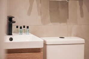 Ein Badezimmer mit einem weißen Waschbecken, vier Shampooflaschen und einer weißen Toilette.