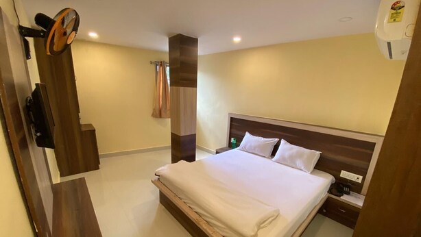 Quarto de hotel com cama, mesa de cabeceira e ventoinha fixada na parede.