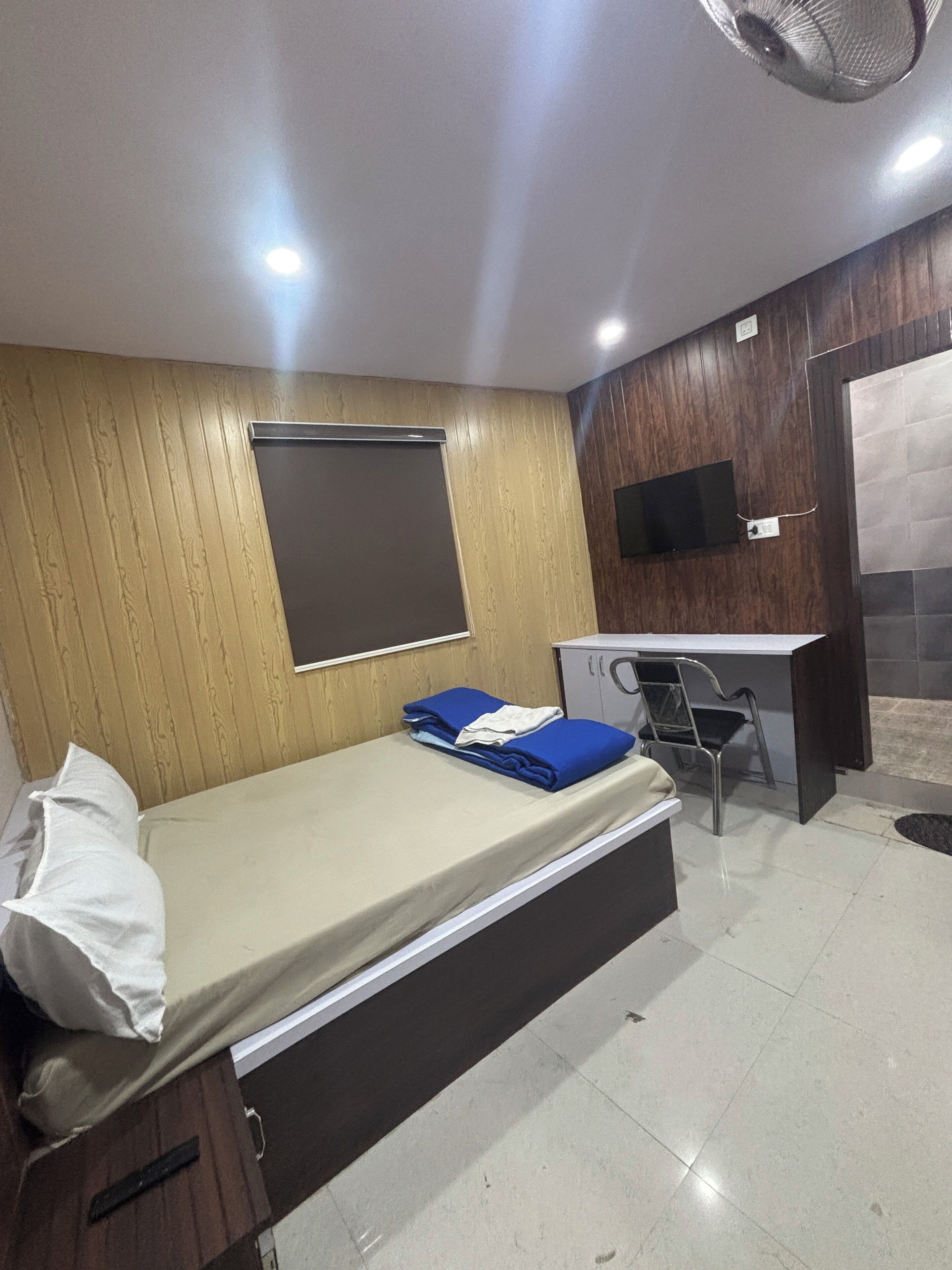 A room with a bed, desk, chair, and a TV mounted on the wall.