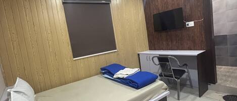 A room with a bed, desk, chair, and a TV mounted on the wall.