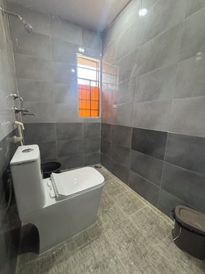 Un baño con inodoro, ducha y ventana con vistas anaranjadas.