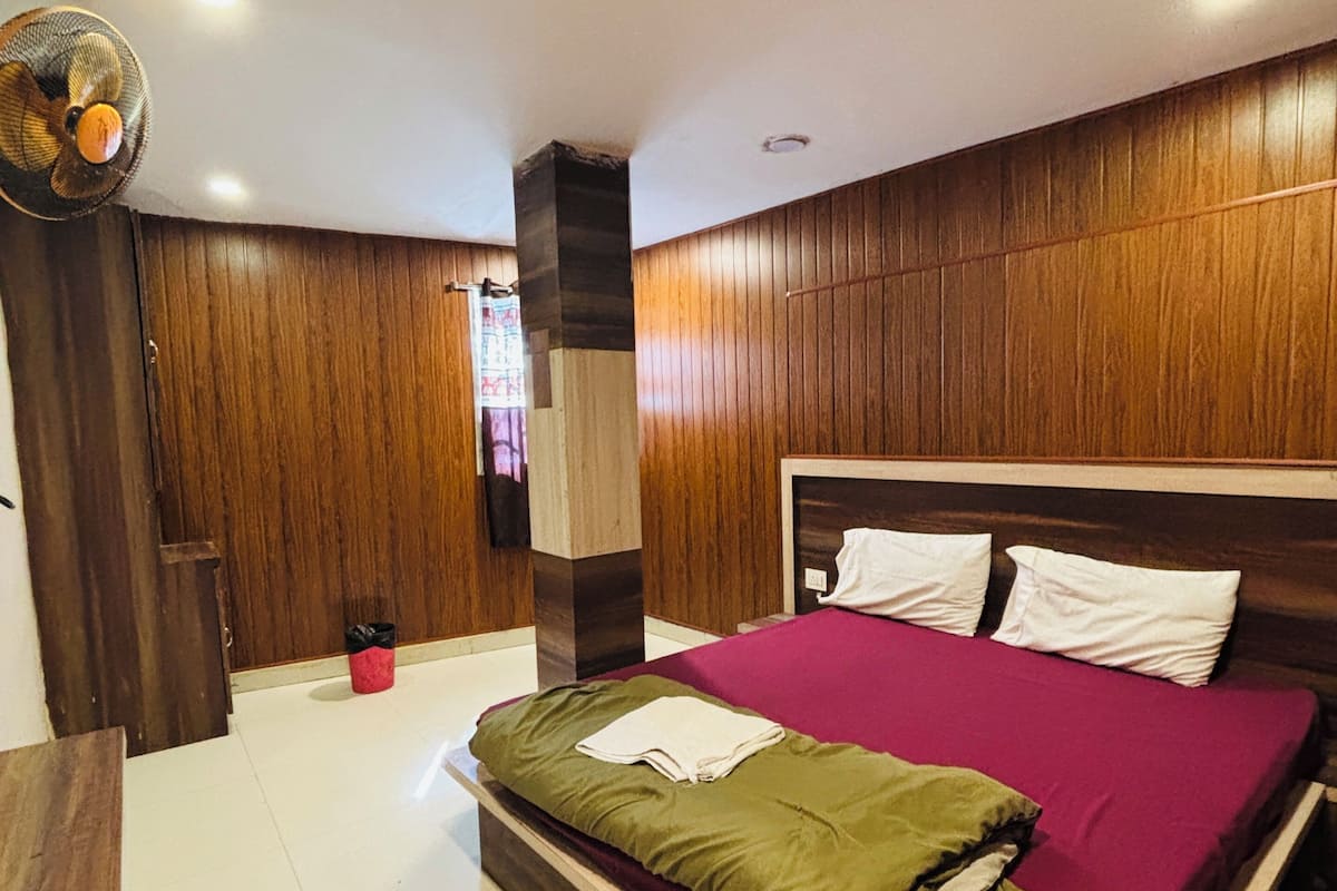 A bedroom with a wooden headboard, a large bed with a purple bedspread, a wooden wardrobe, and a ceiling fan.