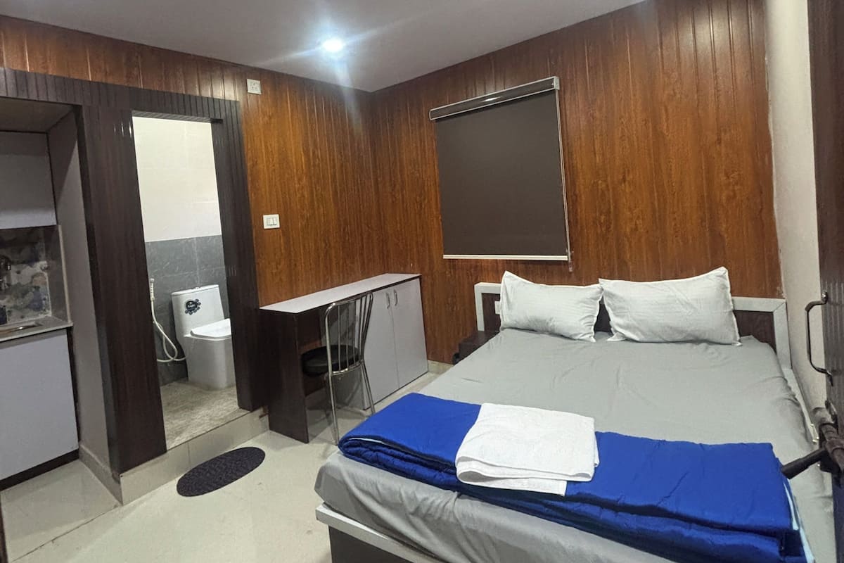 A bedroom with a bed, a desk, a chair, a wardrobe, and a bathroom.
