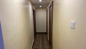 Um corredor estreito com piso de madeira e paredes bege, que leva a uma porta no final.