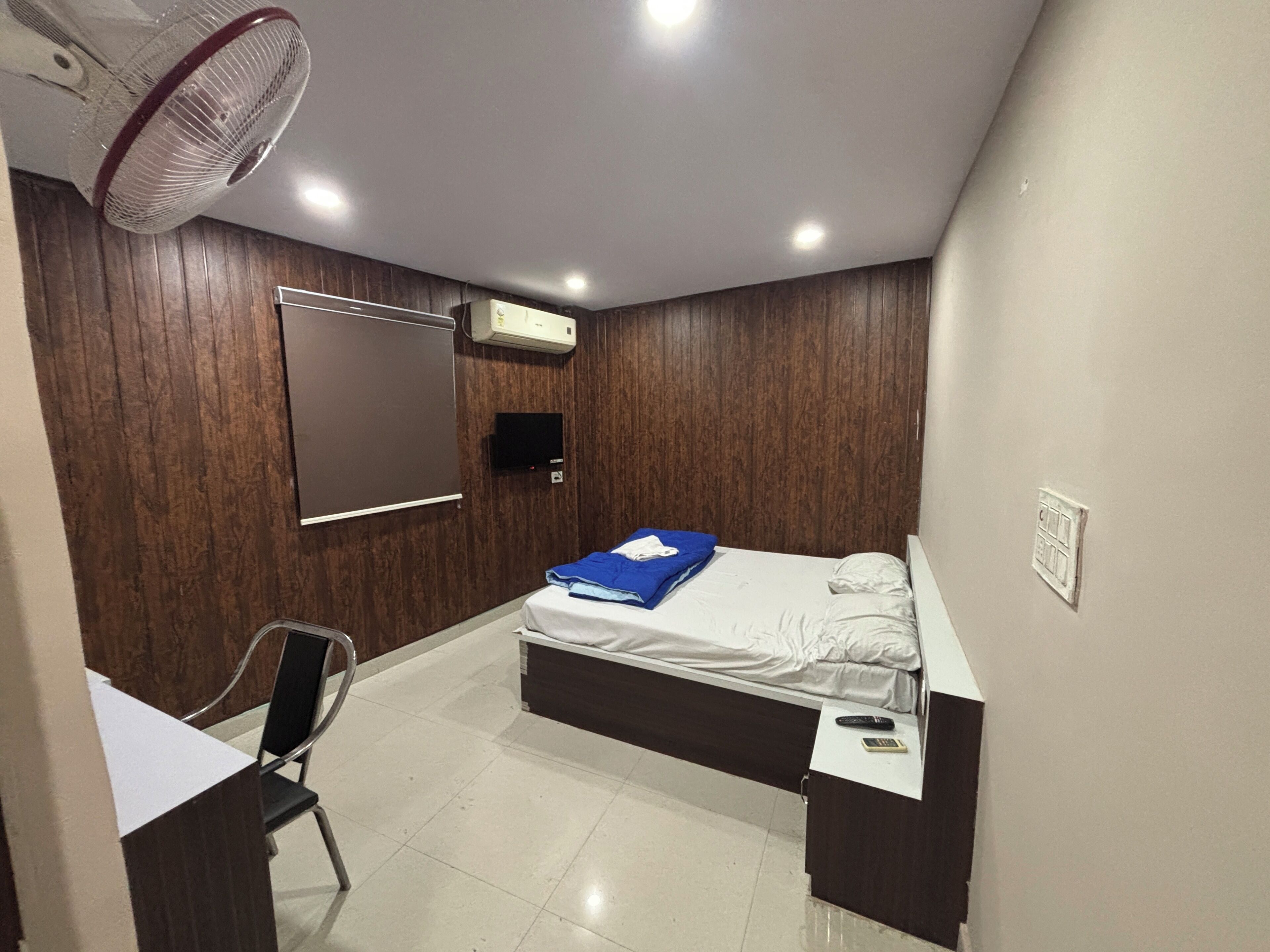 A small, modern bedroom with a bed, a desk, a chair, a TV, and a ceiling fan.