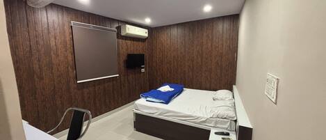 A small, modern bedroom with a bed, a desk, a chair, a TV, and a ceiling fan.