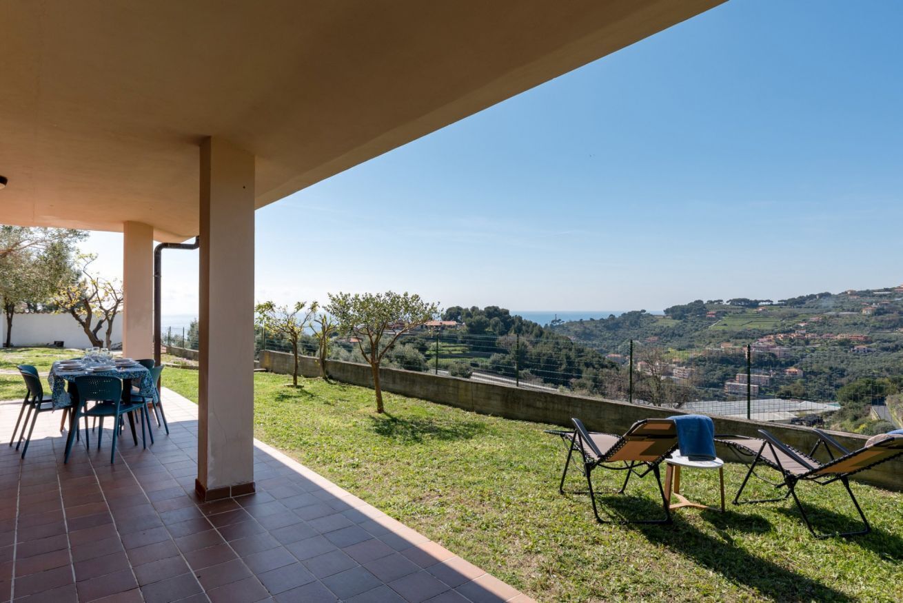 A covered patio with a table and chairs, a lounge area with chairs, and a view of a hilly landscape.