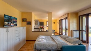 A hotel room with a bed, a TV, a kitchenette, and a view of the outdoors. - A welcoming and spacious 100 square meters apartment, perfect for six people, located on the ground floor of a complex of terraced houses.The property is located in San Lorenzo al Mare, in an extremely quiet area surrounded by nature: the typical Liguria (San Lorenzo al Mare)
