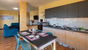 A modern kitchen with dark cabinets, a dining area with blue chairs, and a living room with a blue sofa. - A welcoming and spacious 100 square meters apartment, perfect for six people, located on the ground floor of a complex of terraced houses.The property is located in San Lorenzo al Mare, in an extremely quiet area surrounded by nature: the typical Liguria (San Lorenzo al Mare)