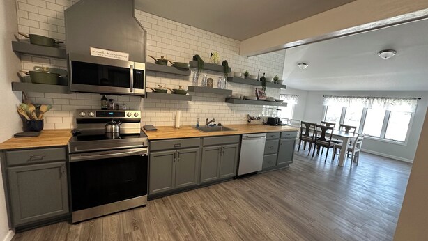 A modern kitchen with a stainless steel range, microwave, and dishwasher, wooden countertops, and a dining area with a table and chairs.