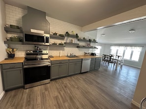 Une cuisine moderne équipée d’une cuisinière, d’un four à micro-ondes et d’un lave-vaisselle en acier inoxydable, de plans de travail en bois et d’un coin repas avec une table et des chaises.