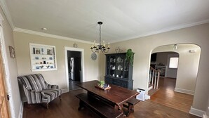 A dining area with a wooden table and benches, a striped armchair, a dark cabinet with glass doors, and a chandelier.
