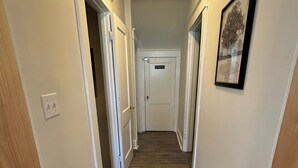 A narrow hallway with wooden flooring, white walls, and doors leading to other rooms.